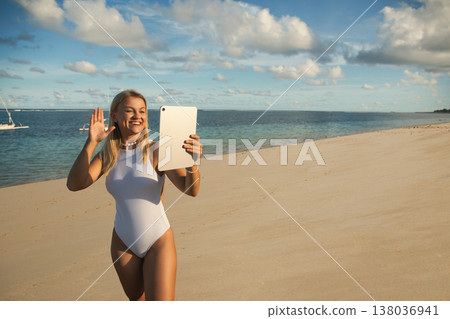 Woman waving while taking a picture with a tablet on the beach 138036941