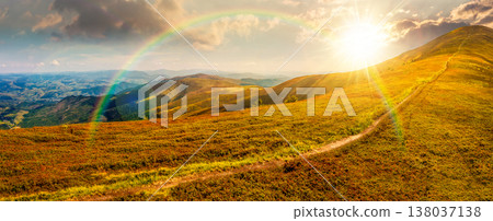 sunset over panorama of a beautiful summer landscape. mountain path through the grassy alpine meadow turns uphill to the sky. distant rolling hills. remote vista under the rainbow sunset over panorama of a beautiful summer landscape. mountain path through the grassy alpine meadow turns uphill to the sky. distant rolling hills. remote vista under the rainbow 138037138
