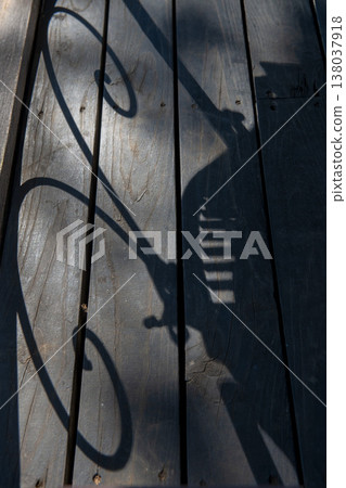 The shadow of the chair stretches across the wooden deck. 138037918