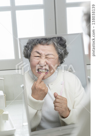 A senior woman becomes concerned about her gums while brushing her teeth. A senior woman becomes concerned about her gums while brushing her teeth. 138038139