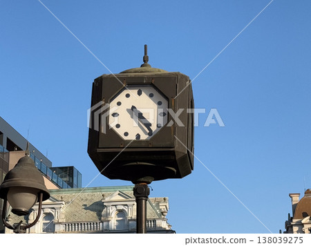 Historic street clock on a metal post rising above classical city architecture under a cloudless sky. Urban timekeeping, heritage streetscape, and old town landmark detail in bright daylight 138039275