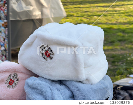 White faux fur Serbian hat ushanka with national coat of arms badge at a street stall. Winter souvenir fashion, patriotic symbolism, and soft textile merchandising in outdoor market light White faux fur Serbian hat ushanka with national coat of arms badge at a street stall. Winter souvenir fashion, patriotic symbolism, and soft textile merchandising in outdoor market light 138039276