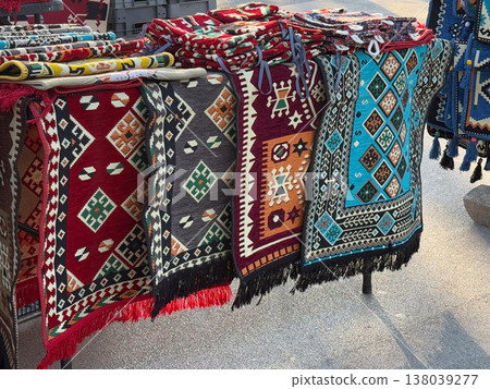 Traditional Serbian woven rugs with geometric motifs displayed at an outdoor market stall. Folk textile craft, ethnic ornament, handmade decor, and cultural shopping in a vibrant street fair setting Traditional Serbian woven rugs with geometric motifs displayed at an outdoor market stall. Folk textile craft, ethnic ornament, handmade decor, and cultural shopping in a vibrant street fair setting 138039277
