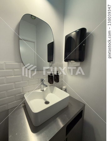 Modern restroom sink area with mirror, faucet, soap dispensers, and paper towel unit. Hygiene maintenance, public bathroom design, sanitation routine, and functional interior organization for daily 138039347