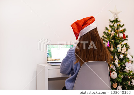 Girl working on laptop computer in Santa hat in Christmas office. Girl working on laptop computer in Santa hat in Christmas office. 138040393