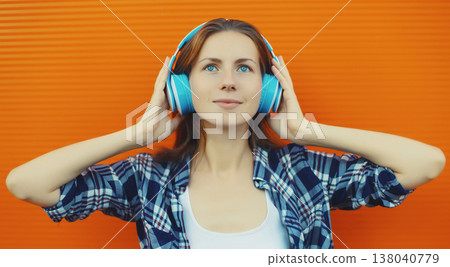 Summer portrait happy modern young woman listening to music with headphones on orange background 138040779