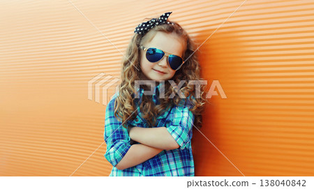 Happy kid girl with curly hair, stylish little child posing in the city on orange wall Happy kid girl with curly hair, stylish little child posing in the city on orange wall 138040842