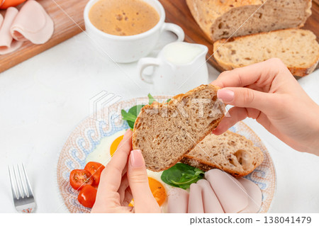Hands Holding Bread Slice over Breakfast Plate with Eggs and Coffee Hands Holding Bread Slice over Breakfast Plate with Eggs and Coffee 138041479