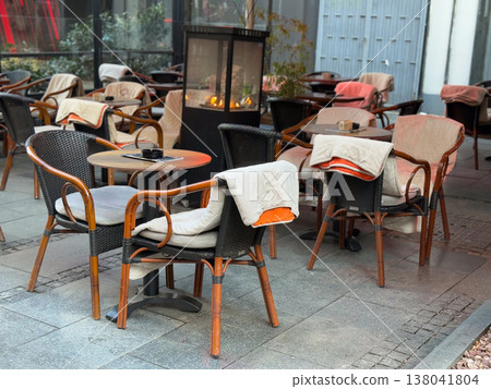Outdoor restaurant terrace with chairs blankets and heater fireplace in evening setting. Seasonal dining adaptation, warmth solution, customer comfort, hospitality design, autumn winter service Outdoor restaurant terrace with chairs blankets and heater fireplace in evening setting. Seasonal dining adaptation, warmth solution, customer comfort, hospitality design, autumn winter service 138041804