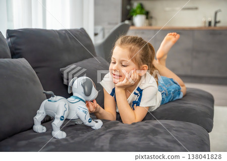 Child hugging robotic dog with affection while sitting on sofa at home. Emotional attachment and digital companionship in modern family life. Child hugging robotic dog with affection while sitting on sofa at home. Emotional attachment and digital companionship in modern family life. 138041828