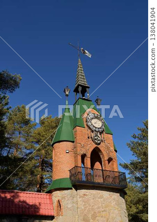 Ancient Brickbuilt Tower Featuring Ornamental Weather Vane Set Against Clear Blue Sky And Tall Pine Trees Ancient Brickbuilt Tower Featuring Ornamental Weather Vane Set Against Clear Blue Sky And Tall Pine Trees 138041904