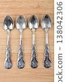 A top view of four vintage metal teaspoons arranged vertically on a wooden surface. 138042306