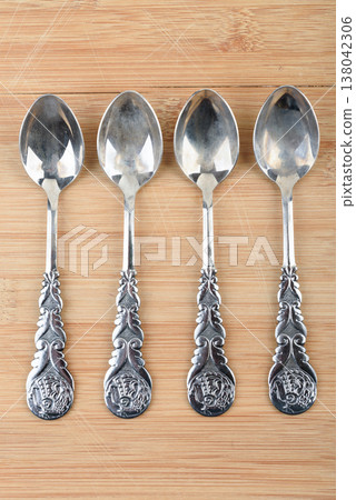 A top view of four vintage metal teaspoons arranged vertically on a wooden surface. 138042306