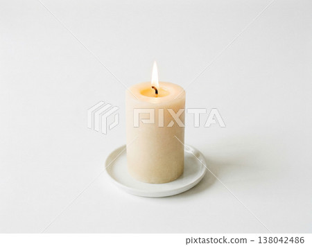 Lit white pillar candle on a small saucer, glowing gently on a white background, home decor 138042486