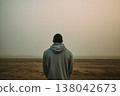 Solitary Man in Hoodie Standing on Empty Beach at Dusk Facing Calm Horizon 138042673