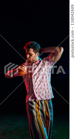 Stylish man drinking beverage in colorful neon lighting isolated on dark background. 138042689