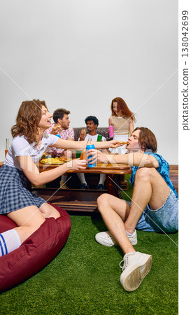 Group of friends sharing fast food and drinks sitting on grass with low table. 138042699