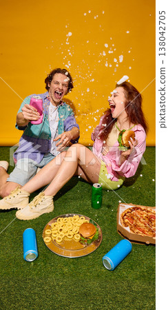 Young couple laughing with splashing drink and fast food on grass bright yellow background. 138042705