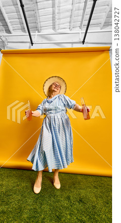 Elderly woman dancing and holding bottled drinks on bright studio yellow background. Elderly woman dancing and holding bottled drinks on bright studio yellow background. 138042727