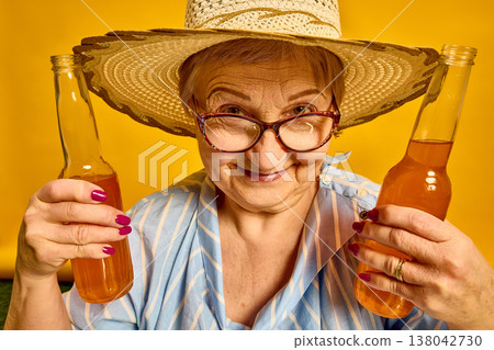 Elderly woman smiling and holding bottled drinks close up on vibrant yellow background. 138042730