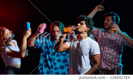 Young friends drinking beverages and having fun under neon studio lighting. 138042764