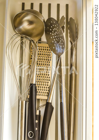 Top-down view of essential stainless steel kitchen utensils neatly organized in a white modern kitchen drawer Top-down view of essential stainless steel kitchen utensils neatly organized in a white modern kitchen drawer 138042922