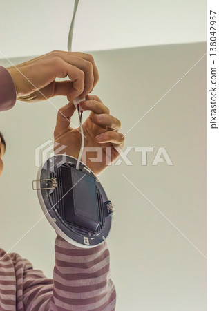 Close up of an electrician's hands connecting wires for a new LED ceiling light. Home improvement and DIY concept. 138042957