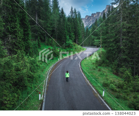 Woman walking on a winding road in lush green forest. Aerial Woman walking on a winding road in lush green forest. Aerial 138044023