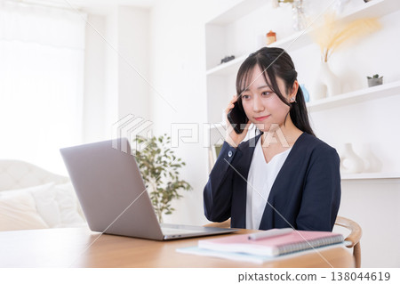 一位二十多歲的女性一邊看著電腦螢幕，一邊用智慧型手機通話。 138044619