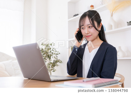 一位二十多歲的女性一邊看著電腦螢幕，一邊用智慧型手機通話。 138044798