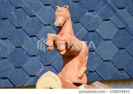 Traditional Terracotta Roof Finial Sculpture of a Prancing Horse on a Slate Roof. Traditional Terracotta Roof Finial Sculpture of a Prancing Horse on a Slate Roof. 138044841