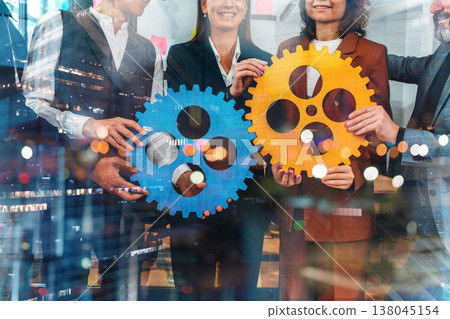Team members hold large blue and orange gears in a modern office setting during a collaborative project meeting 138045154