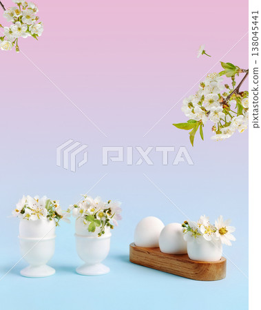 White Easter eggs with funny face with spring pear and strawberry flowers on a pink blue gradient background. Happy Easter concept. Greeting card. White Easter eggs with funny face with spring pear and strawberry flowers on a pink blue gradient background. Happy Easter concept. Greeting card. 138045441