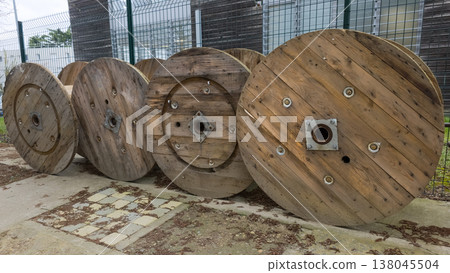 Large wooden cable spools on a construction site. Row of massive empty industrial reels for electrical wire, power cables, and telecommunications infrastructure. Outdoor storage of utility equipment. Large wooden cable spools on a construction site. Row of massive empty industrial reels for electrical wire, power cables, and telecommunications infrastructure. Outdoor storage of utility equipment. 138045504