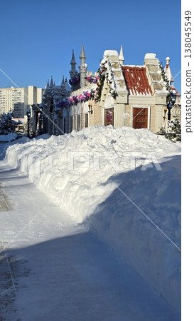 Heavy snowfall creates massive drifts along a path next to a decorated medieval-style building in a sunny winter city park. Heavy snowfall creates massive drifts along a path next to a decorated medieval-style building in a sunny winter city park. 138045549