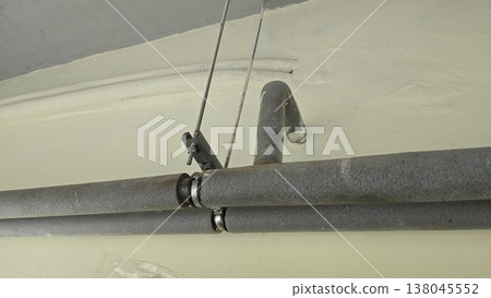 Insulated pipes with gray foam covers are mounted to a ceiling with metal brackets and threaded rods in a utility room. Insulated pipes with gray foam covers are mounted to a ceiling with metal brackets and threaded rods in a utility room. 138045552