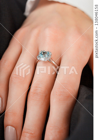 Beautiful female hand with gold ring with diamonds and emerald on gray background Beautiful female hand with gold ring with diamonds and emerald on gray background 138046158