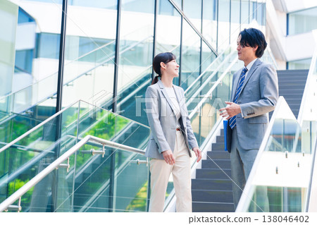 一對男女商務人士一邊走上辦公室的樓梯一邊交談。 138046402