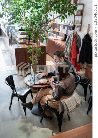 Business meeting at coffee shop, partners discussing project strategy across cups and plants. Business meeting, coffee shop, strategy, partners, teamwork. 138046511