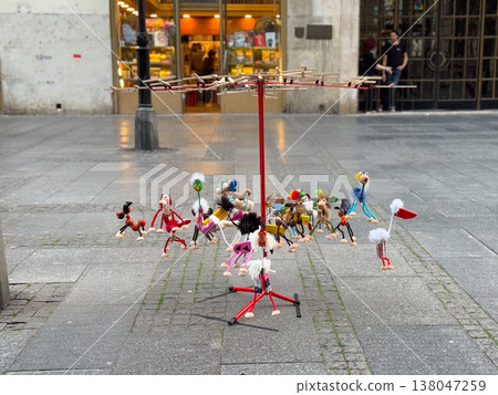Handmade wooden animal toys hanging from a rotating street display in a pedestrian shopping area. Artisan craft retail, playful souvenir merchandising, kinetic design, public market attraction, urban Handmade wooden animal toys hanging from a rotating street display in a pedestrian shopping area. Artisan craft retail, playful souvenir merchandising, kinetic design, public market attraction, urban 138047259