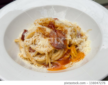 Plate of creamy spaghetti with crispy guanciale grated cheese and egg yolk sauce in white bowl. Italian cuisine, restaurant serving, comfort dining, pasta texture, rich savory meal presentation Plate of creamy spaghetti with crispy guanciale grated cheese and egg yolk sauce in white bowl. Italian cuisine, restaurant serving, comfort dining, pasta texture, rich savory meal presentation 138047276
