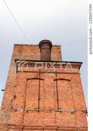 A red brick chimney rises above a historic factory facade A red brick chimney rises above a historic factory facade 138047294