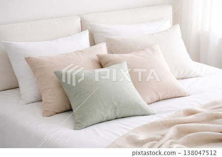 Minimalist bedroom interior with soft neutral pillows and cozy white bedding in natural light 138047512