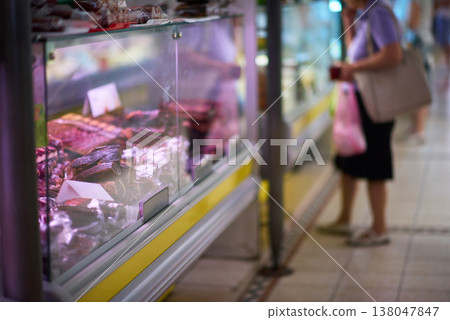 Customer browsing refrigerated deli meat display at a busy indoor market counter Customer browsing refrigerated deli meat display at a busy indoor market counter 138047847