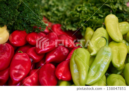 Fresh red and green peppers piled with leafy greens at a market produce display 138047851