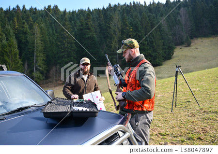 Hunters preparing rifle and targets beside a pickup truck on a forested hillside shooting range Hunters preparing rifle and targets beside a pickup truck on a forested hillside shooting range 138047897