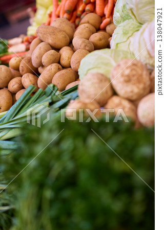 Fresh potatoes and vegetables displayed at a farmers market stall with vibrant greens and carrots 138047921