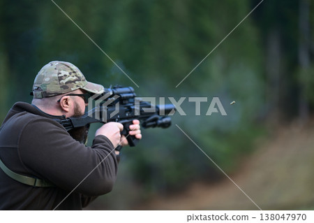 Man in camouflage cap aiming rifle at outdoor shooting range with spent shell ejecting Man in camouflage cap aiming rifle at outdoor shooting range with spent shell ejecting 138047970
