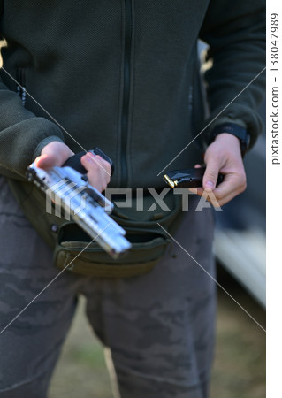 Person loading a handgun magazine outdoors, preparing a pistol for shooting or training Person loading a handgun magazine outdoors, preparing a pistol for shooting or training 138047989
