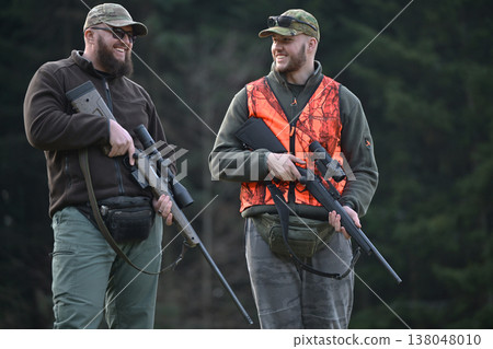 Two hunters walking and laughing in a forest wearing blaze orange vest and camouflage gear Two hunters walking and laughing in a forest wearing blaze orange vest and camouflage gear 138048010